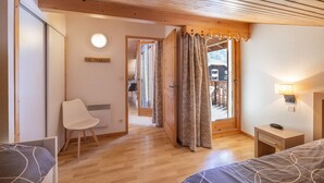 Ein Schlafzimmer mit Holzbalkendecke, einem Bett, einem Sessel, einem Nachttisch mit Lampe und Blick durch eine Tür.