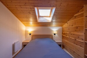 A bedroom with a skylight, a bed, bedside lamps, and a wooden wall. - Apartment for 6/8 in Samoëns – Pools, Balcony & Mountain View (SAMOENS)