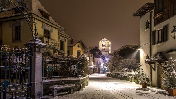 Eine schneebedeckte Straße mit Gebäuden, einem Tor und einem Turm in der Ferne.