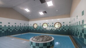 Ein Innenpool mit einer runden Whirlwanne in der Mitte, geflieste Wände und Deckenleuchten.