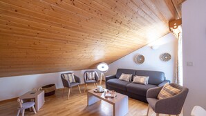Ein modernes Wohnzimmer im Loft-Stil mit schrägem Dach, Holzboden, einer Sofagarnitur, einem Couchtisch und einer Lampe.