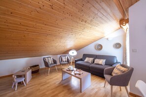 A modern loft-style living room with a sloped ceiling, wooden flooring, a sofa set, a coffee table, and a lamp. - Apartment for 6/8 in Samoëns – Pools, Balcony & Mountain View (SAMOENS)