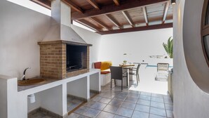 An outdoor kitchen with a brick stove, a sink, and a dining area with chairs and a table.
