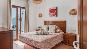 A bedroom with a bed, bedside tables, a wooden headboard, a painting, and a view through a sliding door.