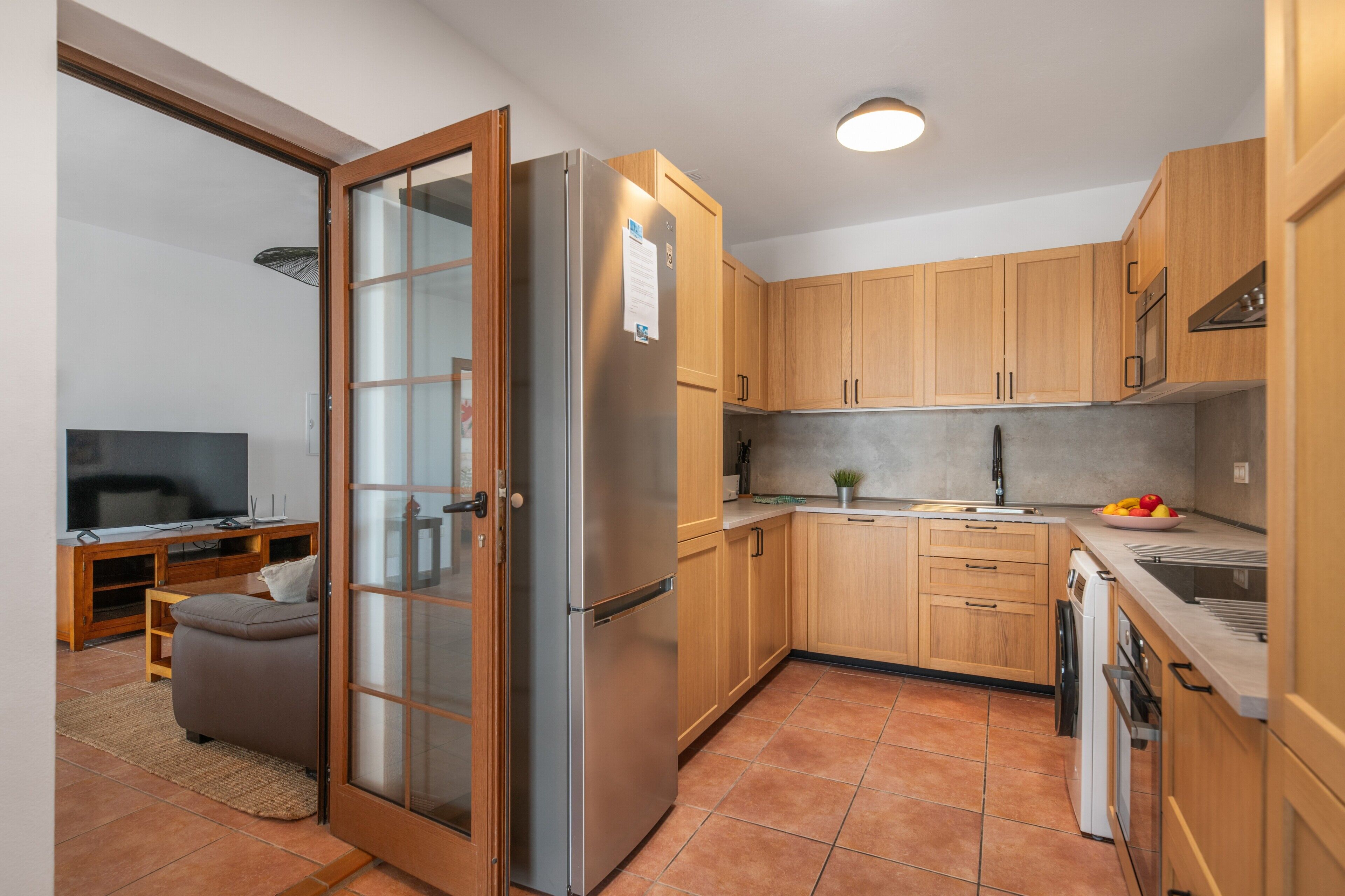 Eine kompakte Küche mit Holzausbau, einem Edelstahlkühlschrank, einem Einbauofen und einem Geschirrspüler.