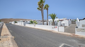 A street with white buildings, palm trees, and a clear sky.