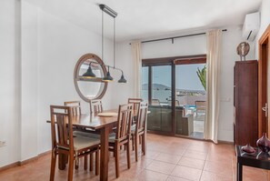 Ein Essbereich mit einem Holztisch und Stühlen, einem großen Spiegel und Blick durch eine Glastür auf einen Außenbereich mit Sitzgelegenheiten.