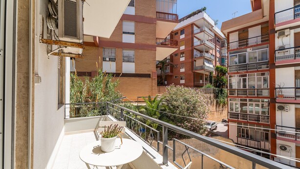 Un balcón con una mesa y sillas, rodeado de edificios con balcones y ventanas.