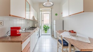 Una cocina estrecha con armarios blancos, una estufa roja y un comedor con mesa y sillas.