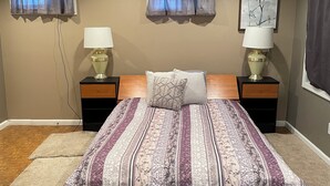 A bedroom with a wooden bed, two bedside lamps, a patterned bedspread, a window with a view, and a painting on the wall. - Studio, sleeps 4, patio, short drive to Ski Resort, Six Flags & concert venues (Ballwin)