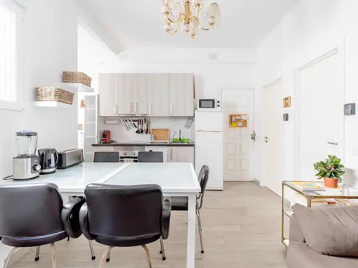 A modern kitchen with white cabinets, a dining table with chairs, a coffee machine, and a microwave.