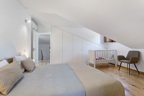 A bedroom with a bed, a crib, a chair, and a wardrobe.