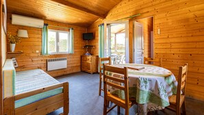 A wooden cabin with a bed, a table with chairs, a television, and a window.