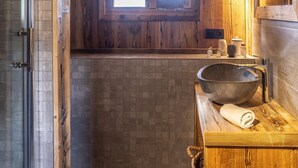 Un baño con tocador de madera, un lavabo grande, una ventana y piso de baldosas.