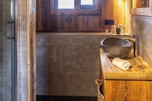 Une salle de bain avec un meuble-lavabo en bois, un grand lavabo en forme de cuve, une fenêtre et un sol carrelé.
