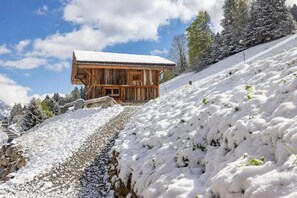 A wooden cabin with a snow-covered roof, situated on a snow-covered slope with a clear sky.