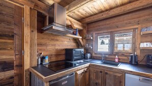 A wooden cabin interior with a kitchen area featuring a stove, oven, and dishwasher. - Chalet 'Mazot Des Aravis' with Mountain View, Private Terrace and Private Garden (Combloux)