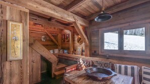 A rustic cabin interior with wooden walls, a fireplace, a dining table with a cast iron skillet, and a window overlooking a snowy landscape. - Chalet 'Mazot Des Aravis' with Mountain View, Private Terrace and Private Garden (Combloux)