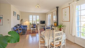 Un salón con una mesa de comedor, sillas, sofá, televisor y ventanas amplias.