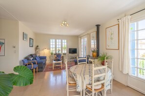 A living room with a dining table, chairs, a sofa, a TV, and large windows.