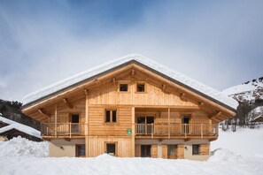 Een houten chalet met balkon, omringd door sneeuw.