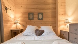 Un dormitorio de cabaña de madera con una cama, dos mesitas de noche con lámparas, un aparador y dos cuadros en la pared.