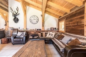 Interno di una baita di legno con soffitto in legno, un divano in pelle, un tavolino da caffè, un orologio e una decorazione con testa di cervo.