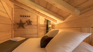 Ein holzgetäfeltes Zimmer im Blockhausstil mit Bett, Kissen, Nachttisch und einer Wandlampe.