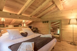 Camera da letto in una baita di legno, con un letto, cuscini, un comodino, uno specchio e una lampada da terra.