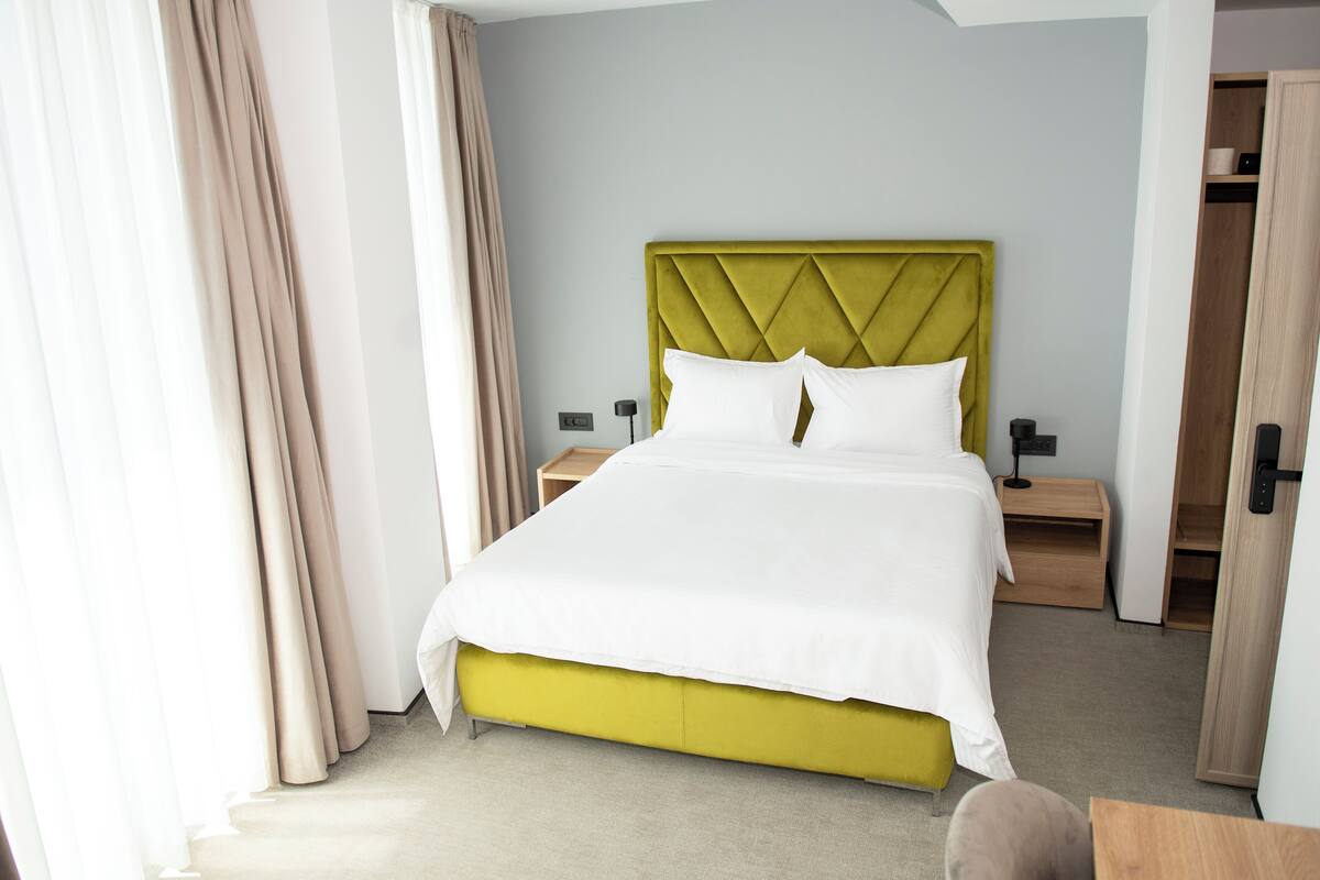 A hotel room with a bed, nightstands, a wardrobe, and a window with curtains.