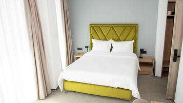 Une chambre d’hôtel avec un lit, des tables de chevet, une armoire et une fenêtre avec des rideaux.