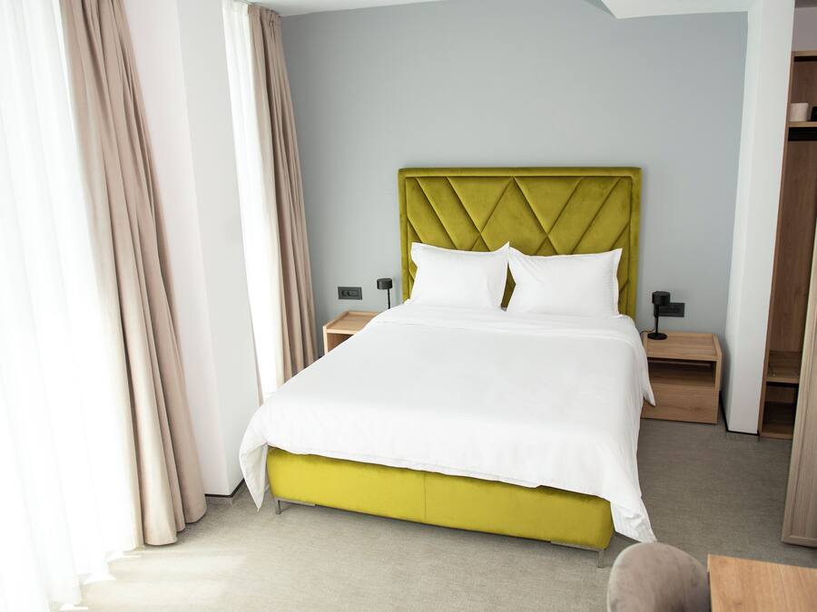 Une chambre d’hôtel avec un lit, des tables de chevet, une armoire et une fenêtre avec des rideaux.