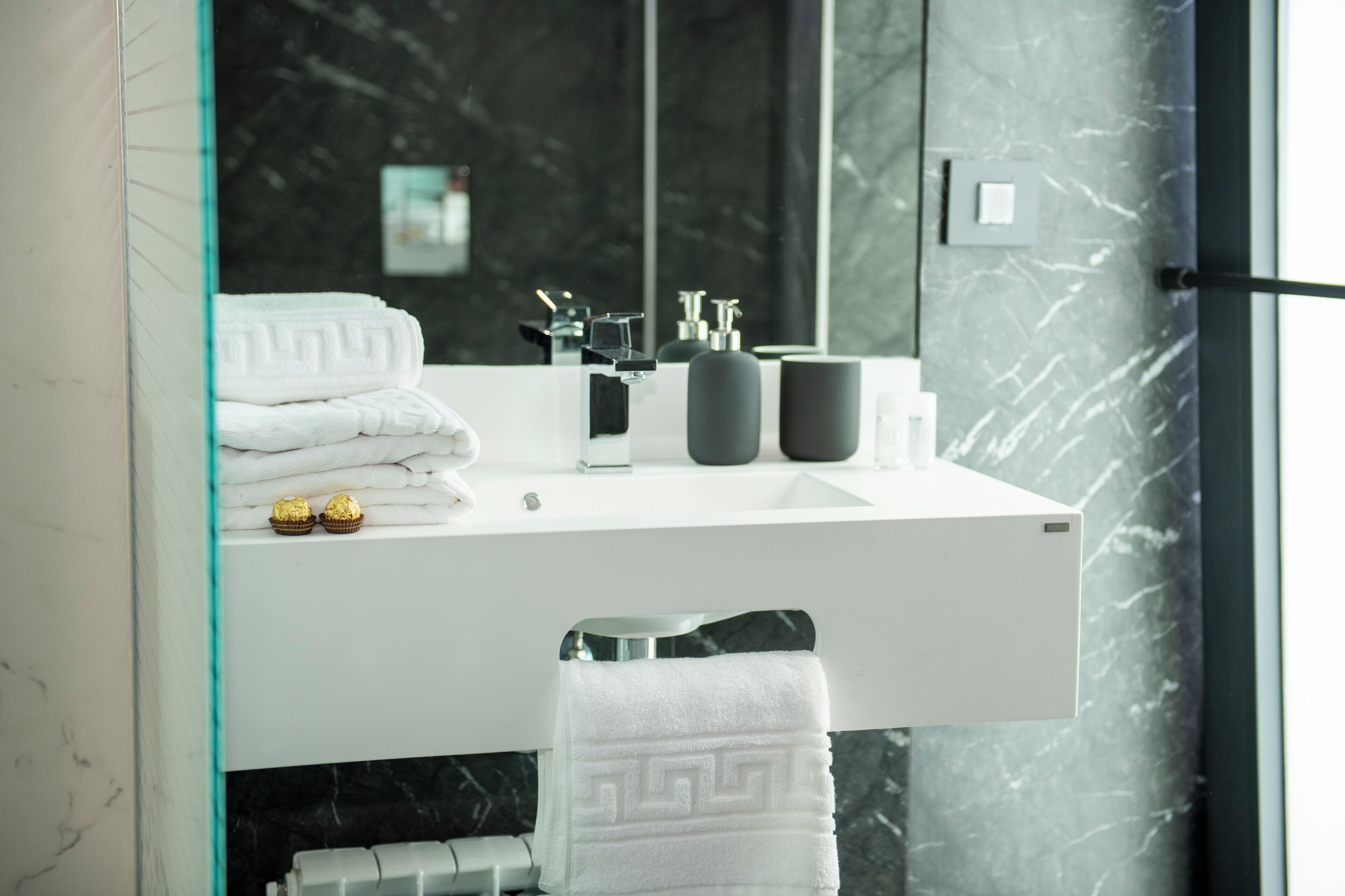 A modern bathroom with a white vanity, black marble backsplash, and a glass shower enclosure.