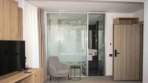 Una habitación moderna con una televisión, una silla, una mesita y una puerta corredera que da a un baño.