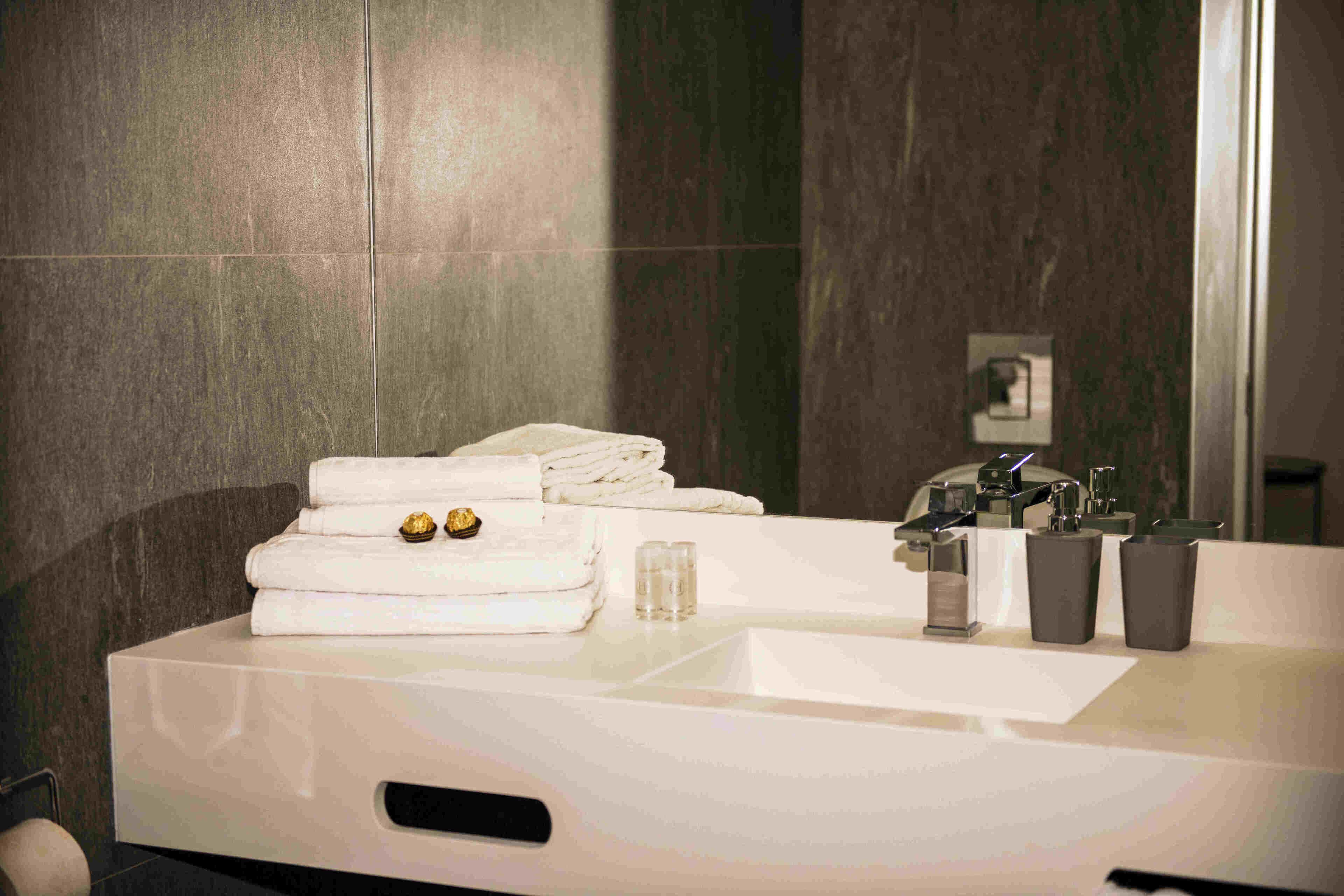 A modern bathroom with a large mirror, a sink, and neatly folded towels on the counter.