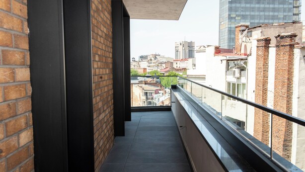 Un estrecho pasillo con paredes de ladrillo y barandilla de vidrio con vistas a un paisaje urbano.