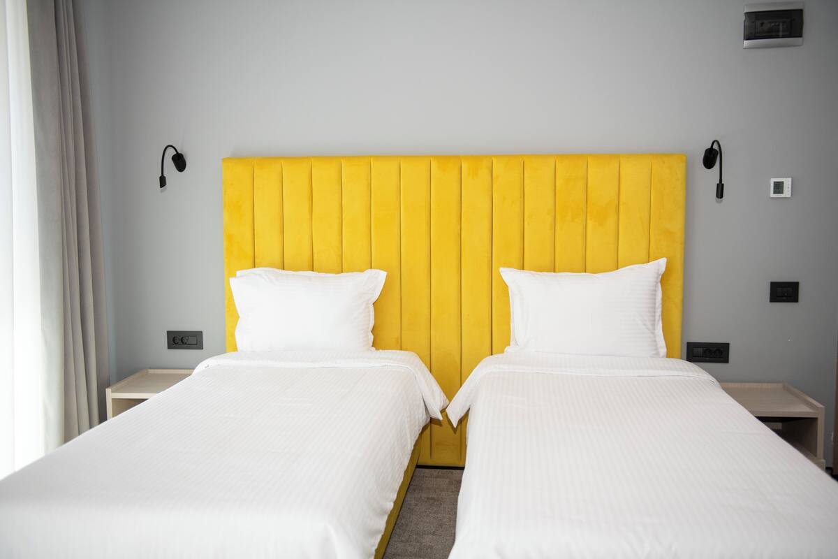 A hotel room with two single beds, a yellow headboard, white bedding, and bedside lamps.