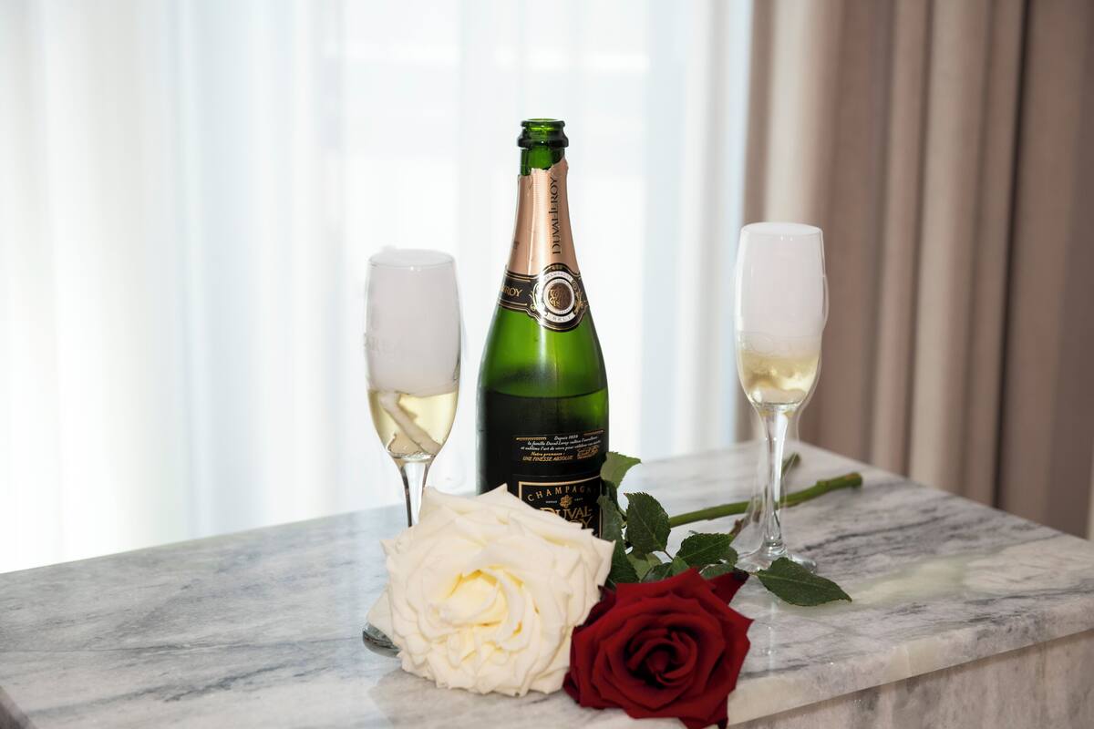 A bottle of champagne, two glasses, and a white and red rose on a marble surface.