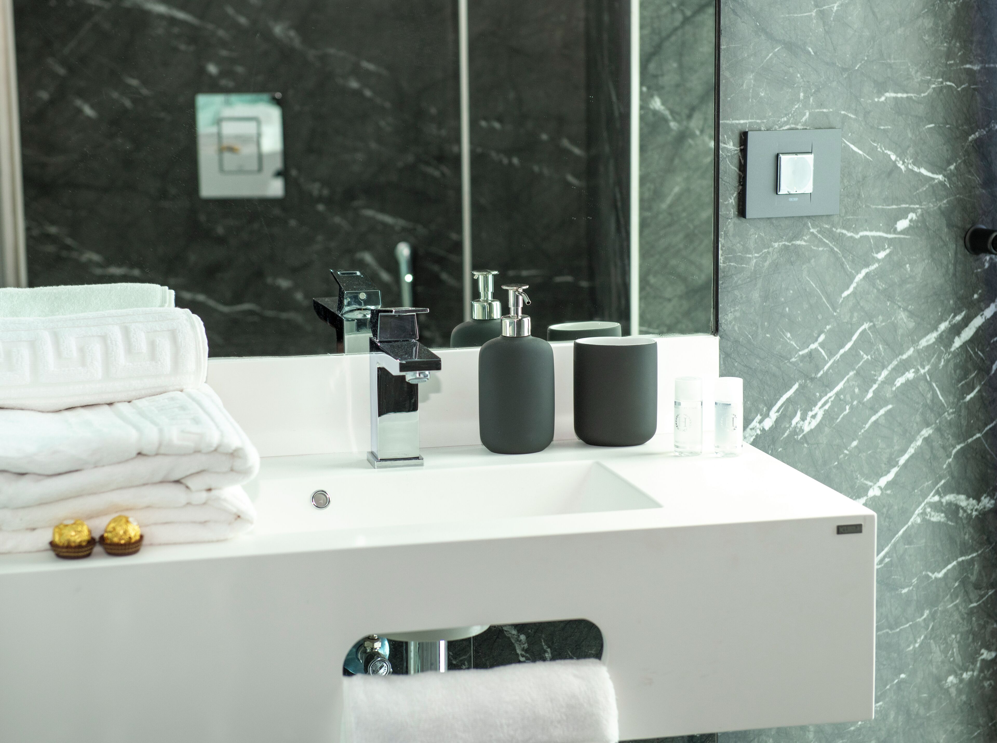 A modern bathroom with a white sink, black marble walls, and a large mirror.