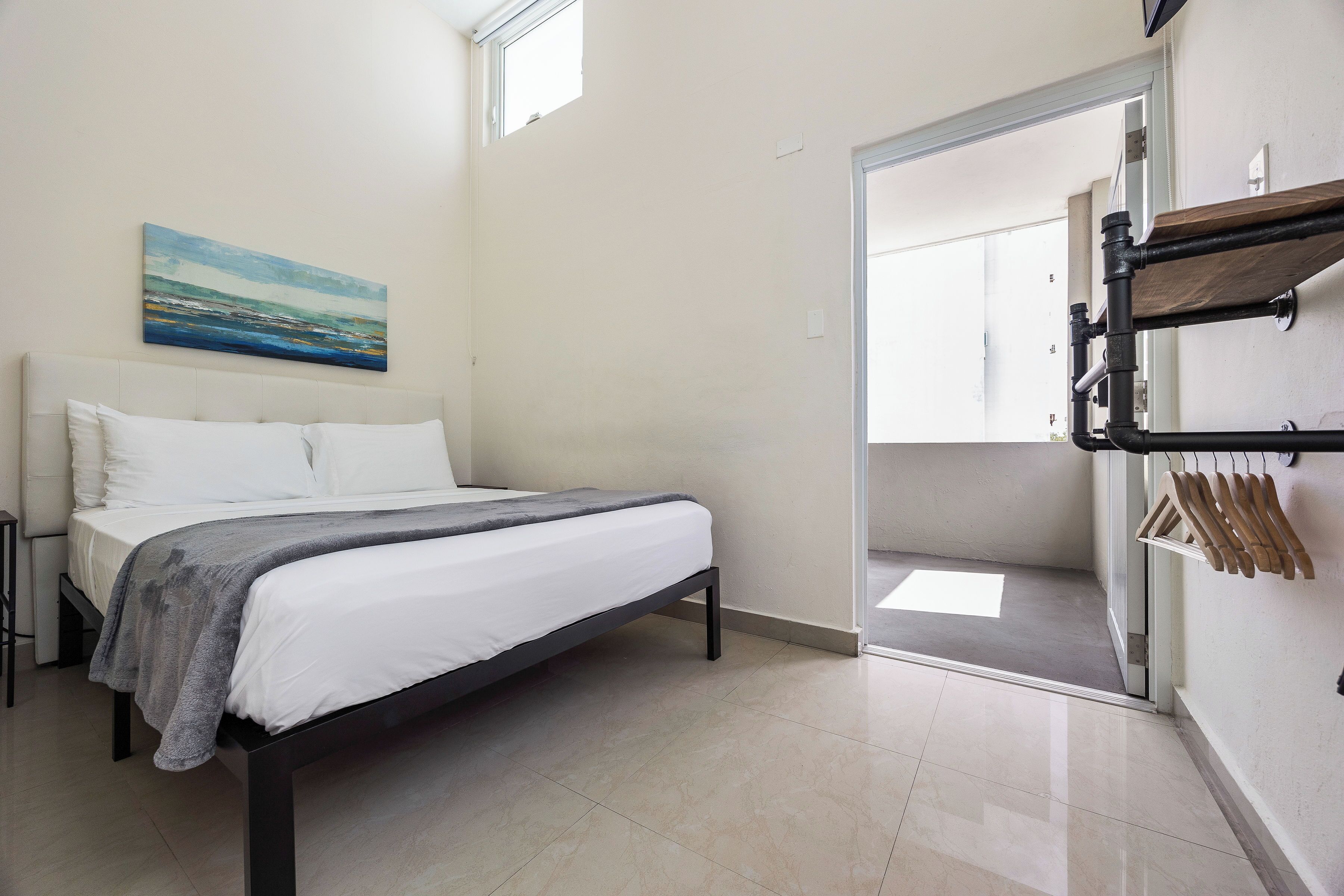 A bedroom with a bed, a painting, a wardrobe, and a door leading to another room.