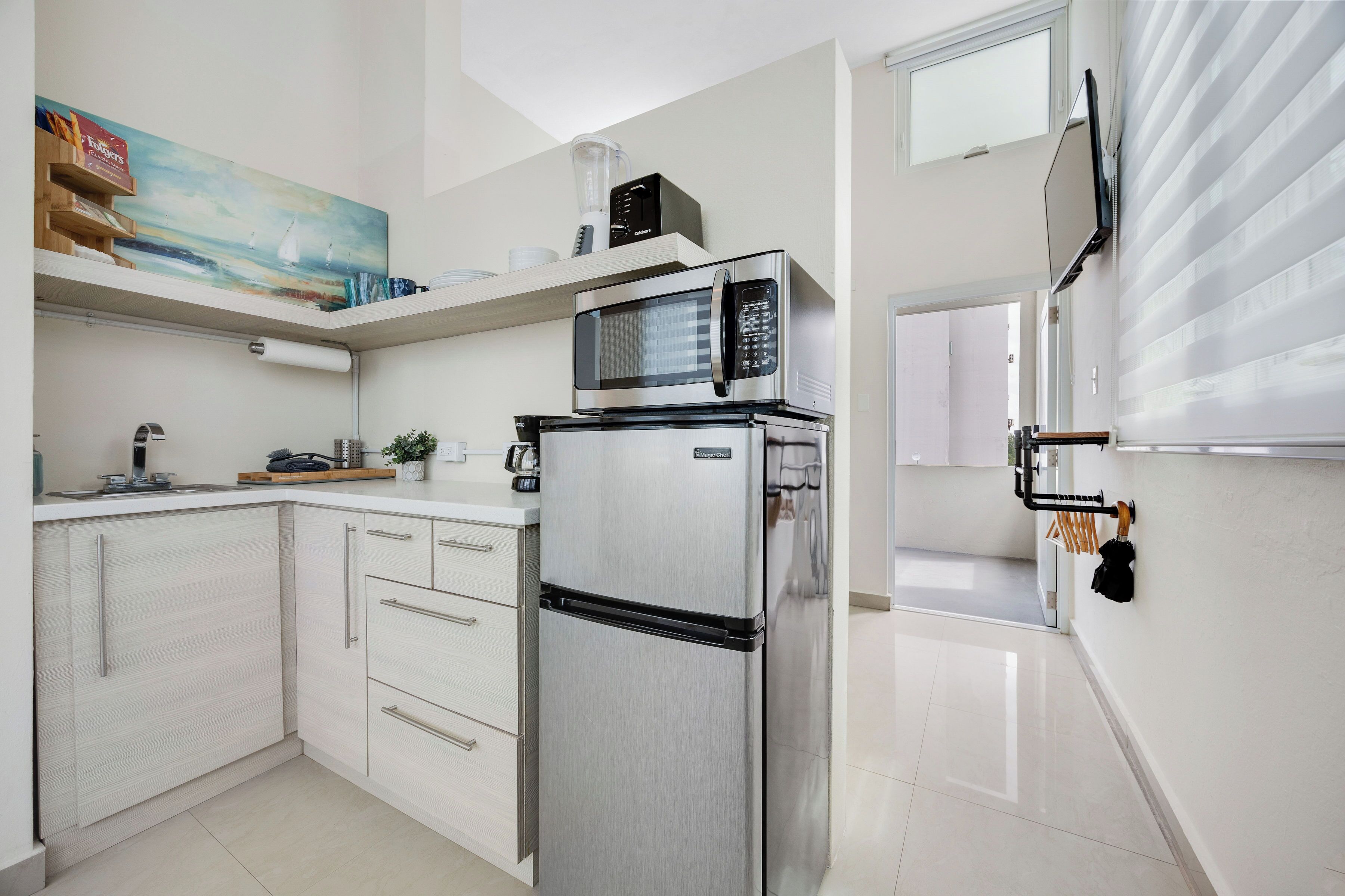 Una cocina moderna con armarios blancos, un refrigerador de acero inoxidable, un microondas y una licuadora en la encimera.