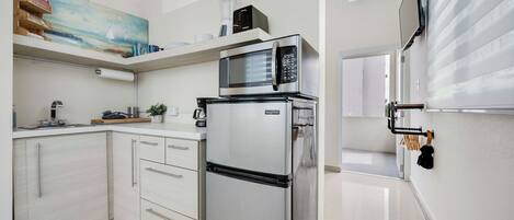 Una cocina moderna con armarios blancos, un refrigerador de acero inoxidable, un microondas y una licuadora en la encimera.