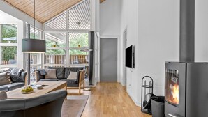 A modern living room with a fireplace, wooden flooring, and a seating area with a sofa and chairs. - Cozy home in Hasle with sauna (Hasle)
