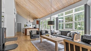 A spacious living area with a wooden ceiling, large windows offering a view of greenery, a central coffee table, and a sofa with cushions. - Cozy home in Hasle with sauna (Hasle)