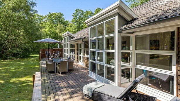 A deck with outdoor furniture, a glass-enclosed patio, and a view of the surrounding greenery. - Cozy home in Hasle with sauna (Hasle)