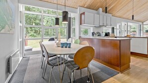 A modern kitchen with large windows, a dining area with a round table and chairs, and a wooden ceiling. - Cozy home in Hasle with sauna (Hasle)