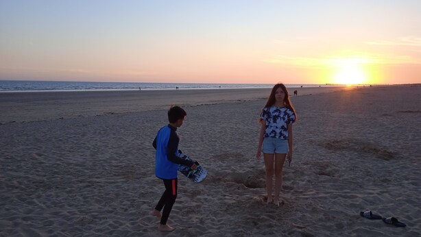 Een strandscène met twee personen, één daarvan houdt een skateboard vast.