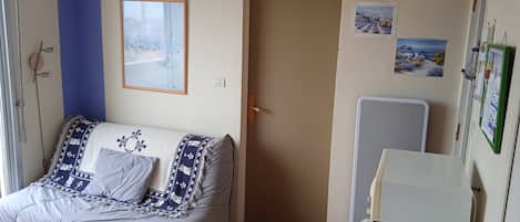 Quarto com cama, porta, ar condicionado fixado na parede e janela com vista para um edifício.