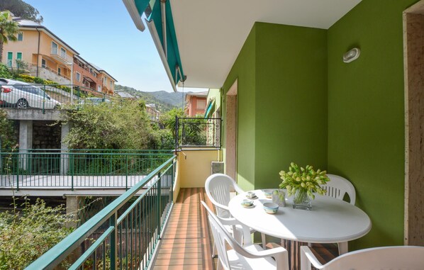 A balcony with a white table and chairs, a small potted plant, and a view of neighboring buildings.