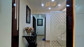 A modern hallway with a dark wooden door frame, a glass console table with a basket of flowers, and a decorative screen with a geometric pattern. - Patio Paradise, Pitampura
Cozy and peaceful 3BHK Condo (New delhi)